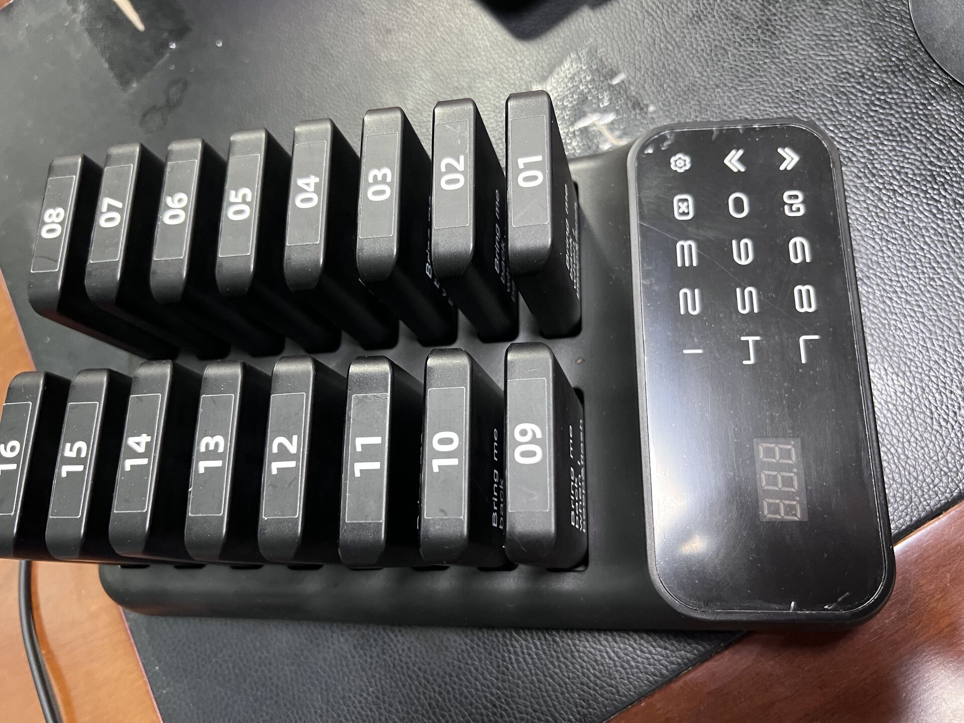 Close-up real photo of a STMITE 16 pager system charging base with numbered guest pagers